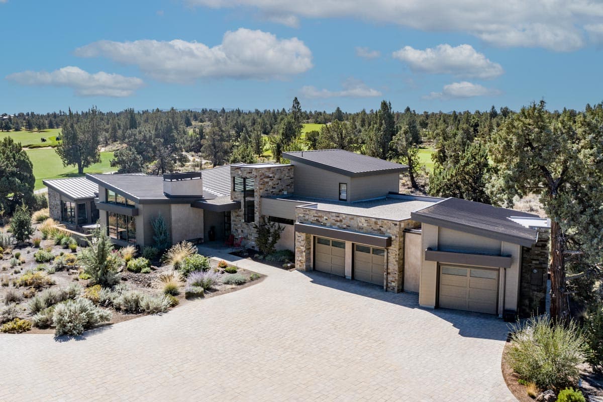 House plan exterior. Modern style, multi-level home with flat and angled rooflines, stone facade, and attached garage. Driveway visible.