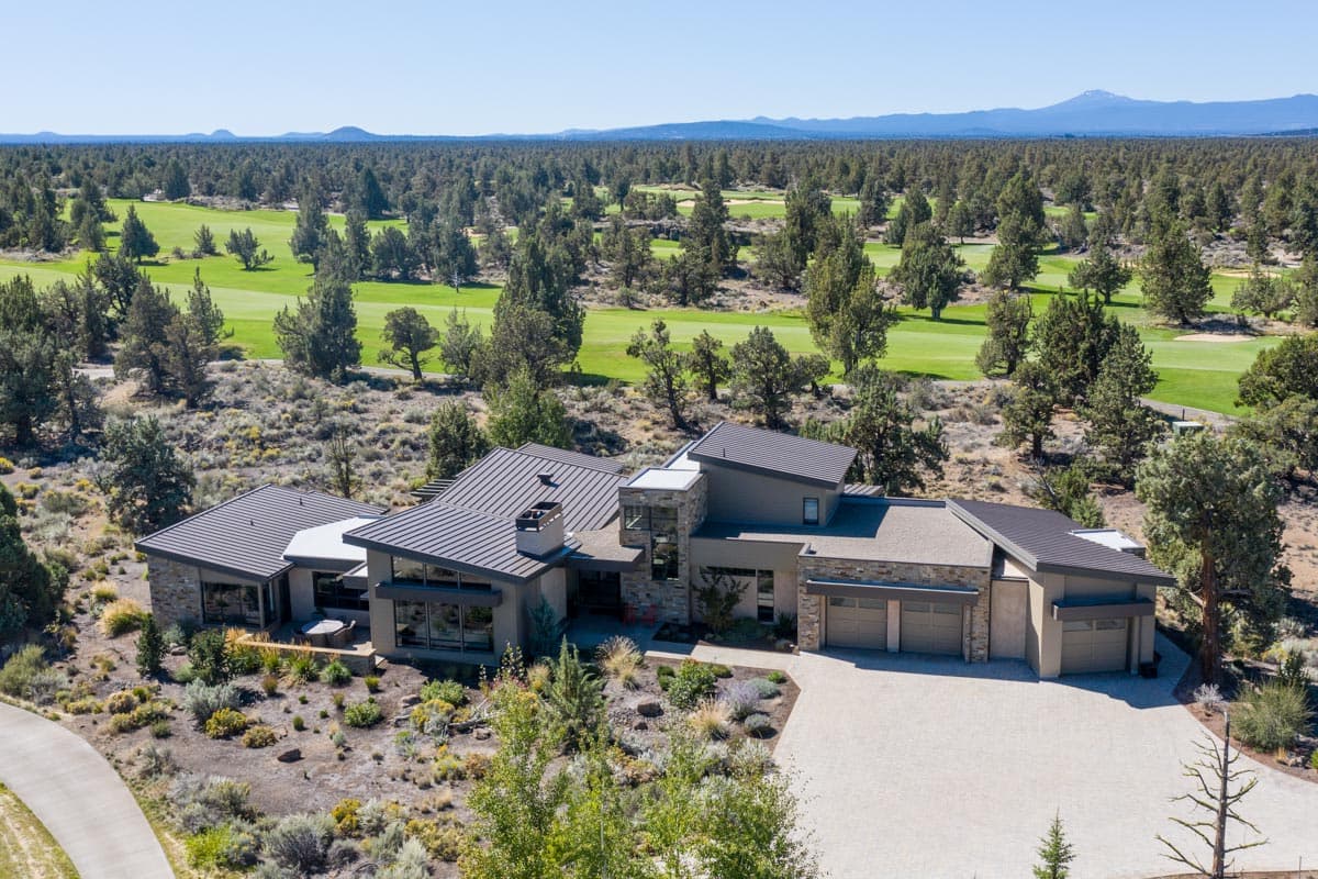 House plan exterior of a modern home with multiple gables, a three-car garage, and extensive glazing, set against a golf course landscape.