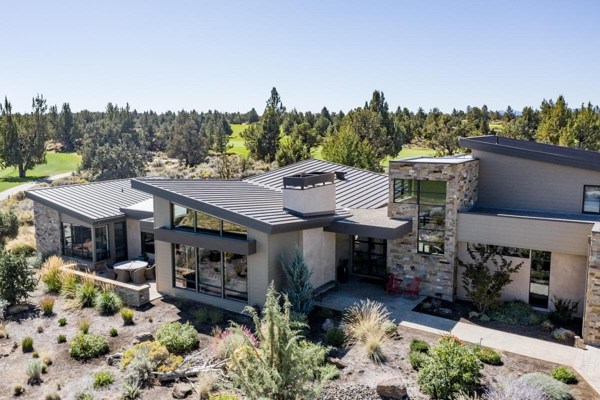 Modern house plan exterior with stone facade, metal roof, large windows, and multi-level rooflines.