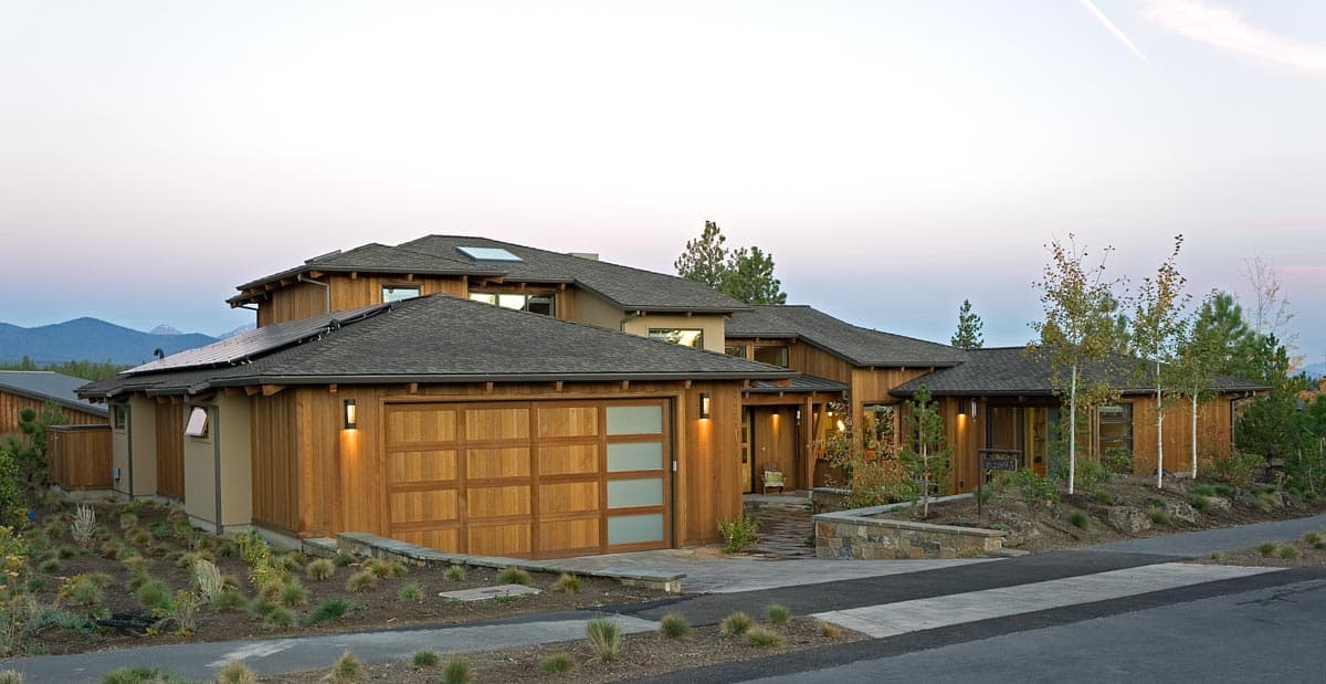 Modern house exterior with wood siding, low-pitched roofs, solar panels, and a multi-panel garage door.