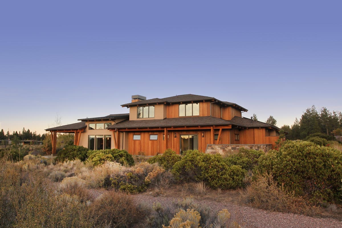 Modern house plan exterior with wood siding, layered rooflines, and large windows. Features a covered entryway and stone accents.