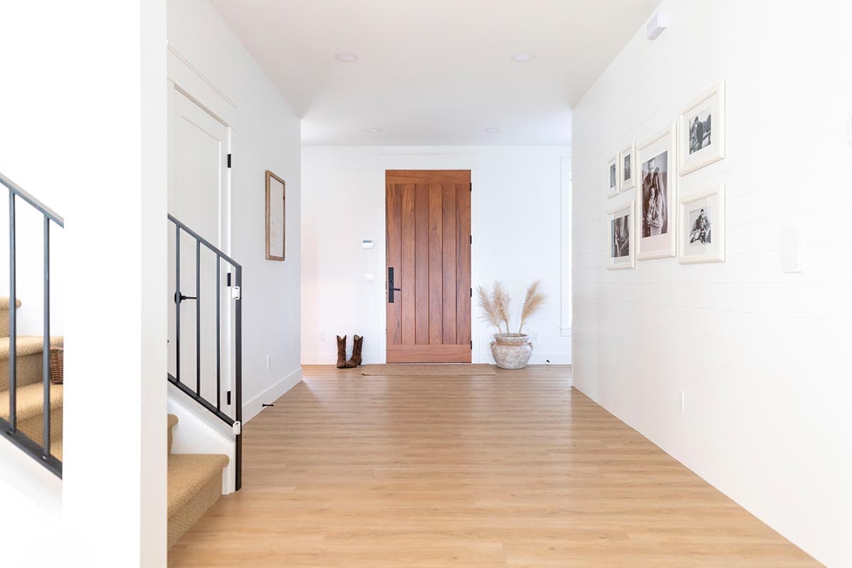 Interior view of a foyer with a wood door, staircase, and wall art.