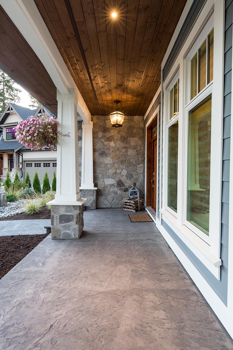 House plan exterior showing covered porch with stone accents, wood ceiling, and large windows.