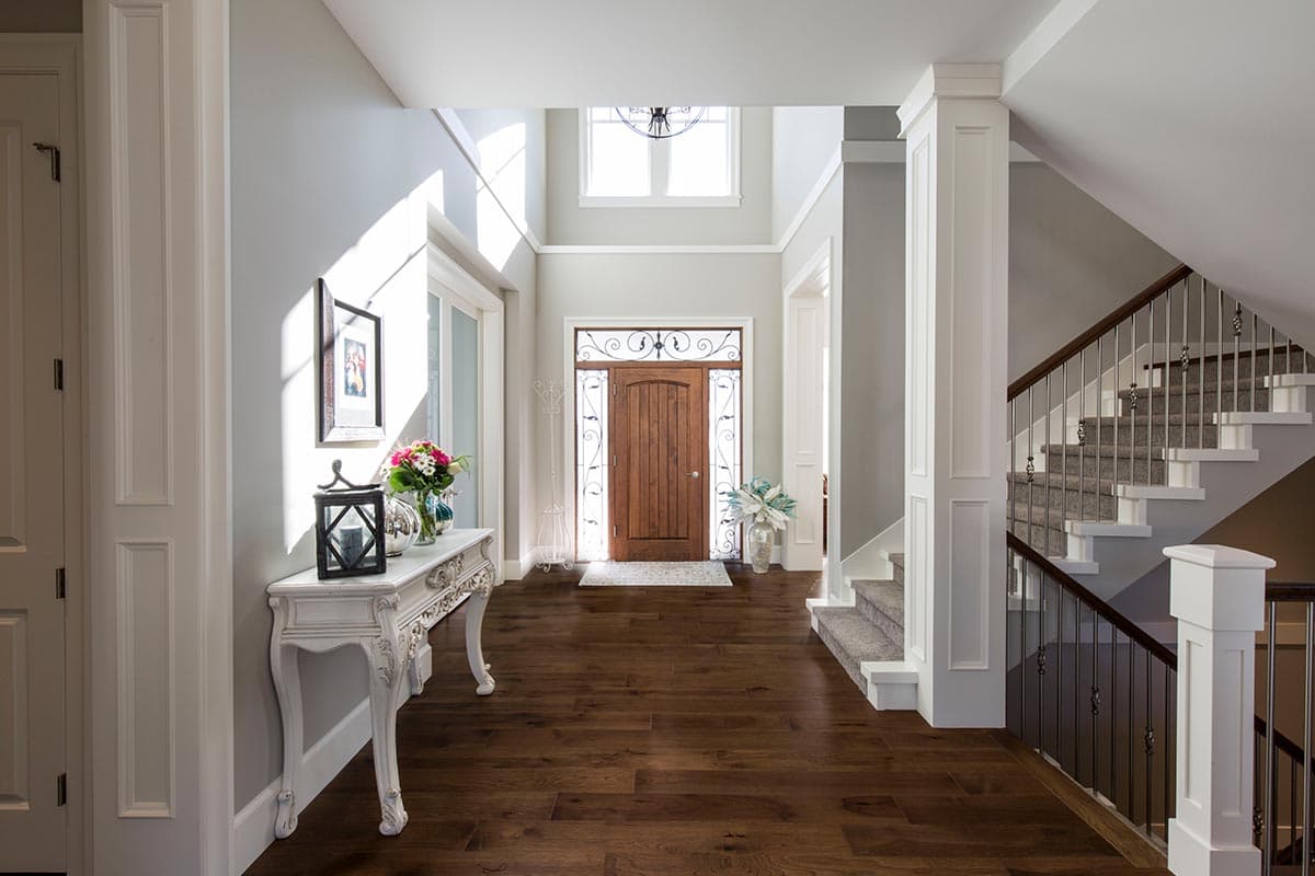 Interior view of a two-story foyer with a grand wooden front door, decorative sidelights, and a carpeted staircase.