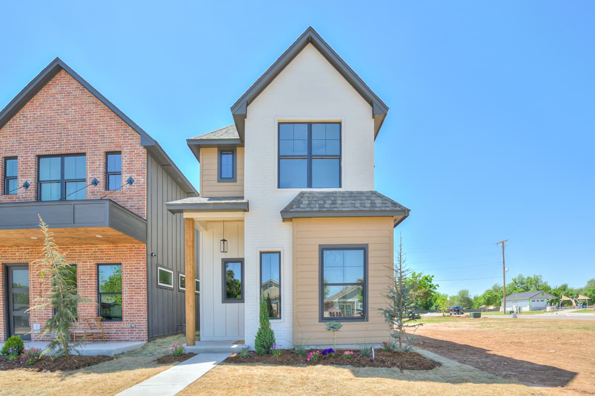 House plan exterior. Two-story home with a gabled roof, a front porch with a wood column, and large windows with black trim.
