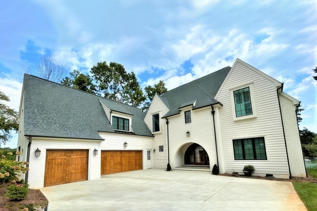 House plan exterior: Modern style with white siding, gables, dormers, arched entryway, and three garage doors.
