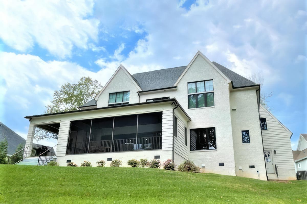 Exterior view of a two-story house plan featuring white brick, gables, a screened porch, and a covered patio.