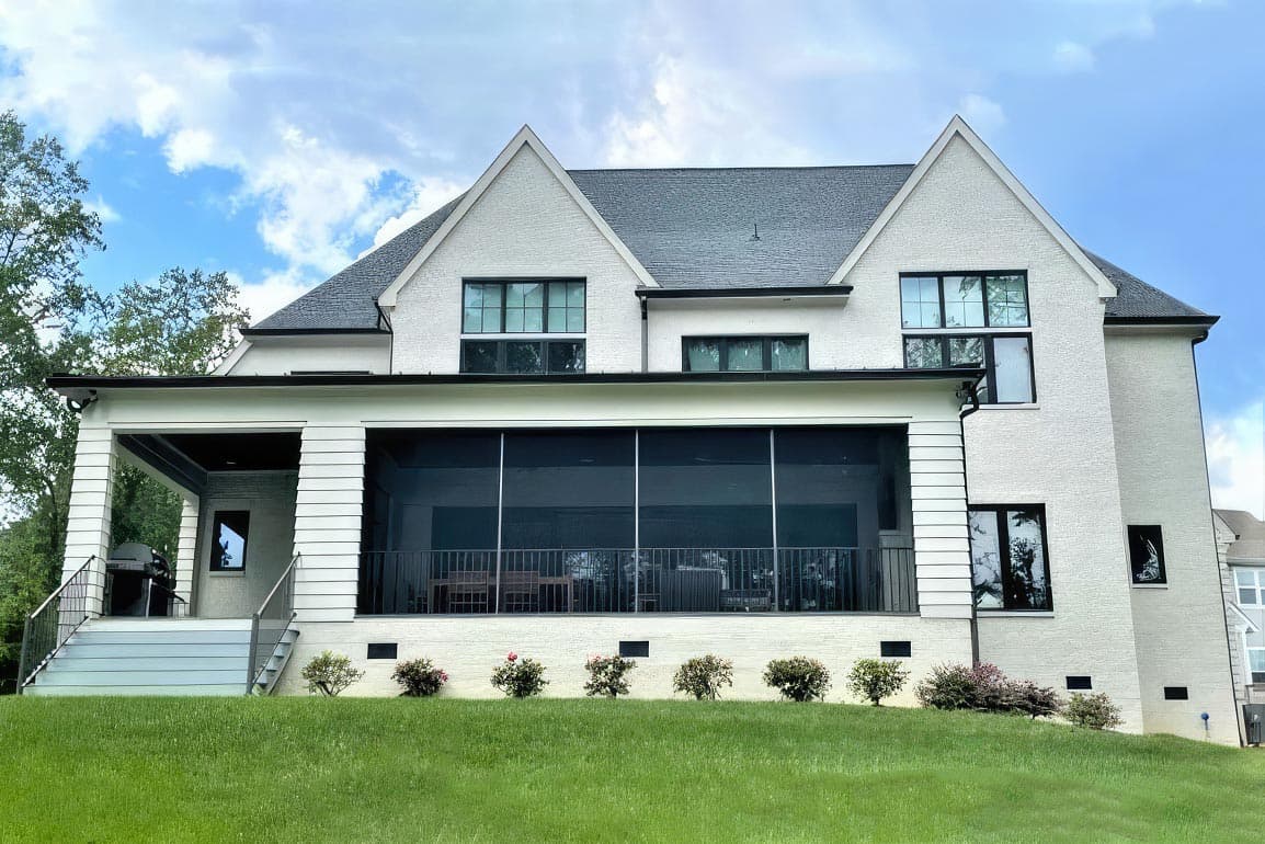 House plan exterior: Two-story, white brick home with multiple gables, a screened-in porch, and a covered deck.