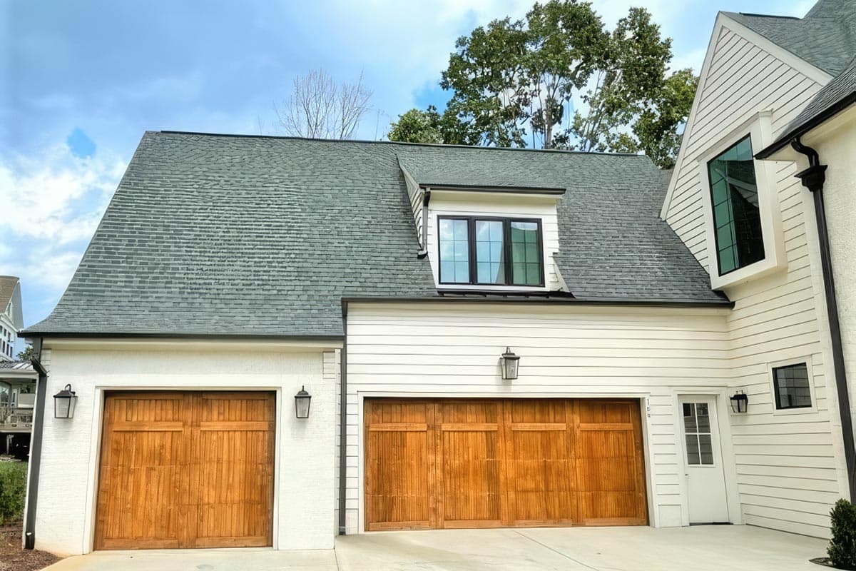 House plan exterior featuring a three-car garage with natural wood doors, a dormer window with black trim, and white siding.
