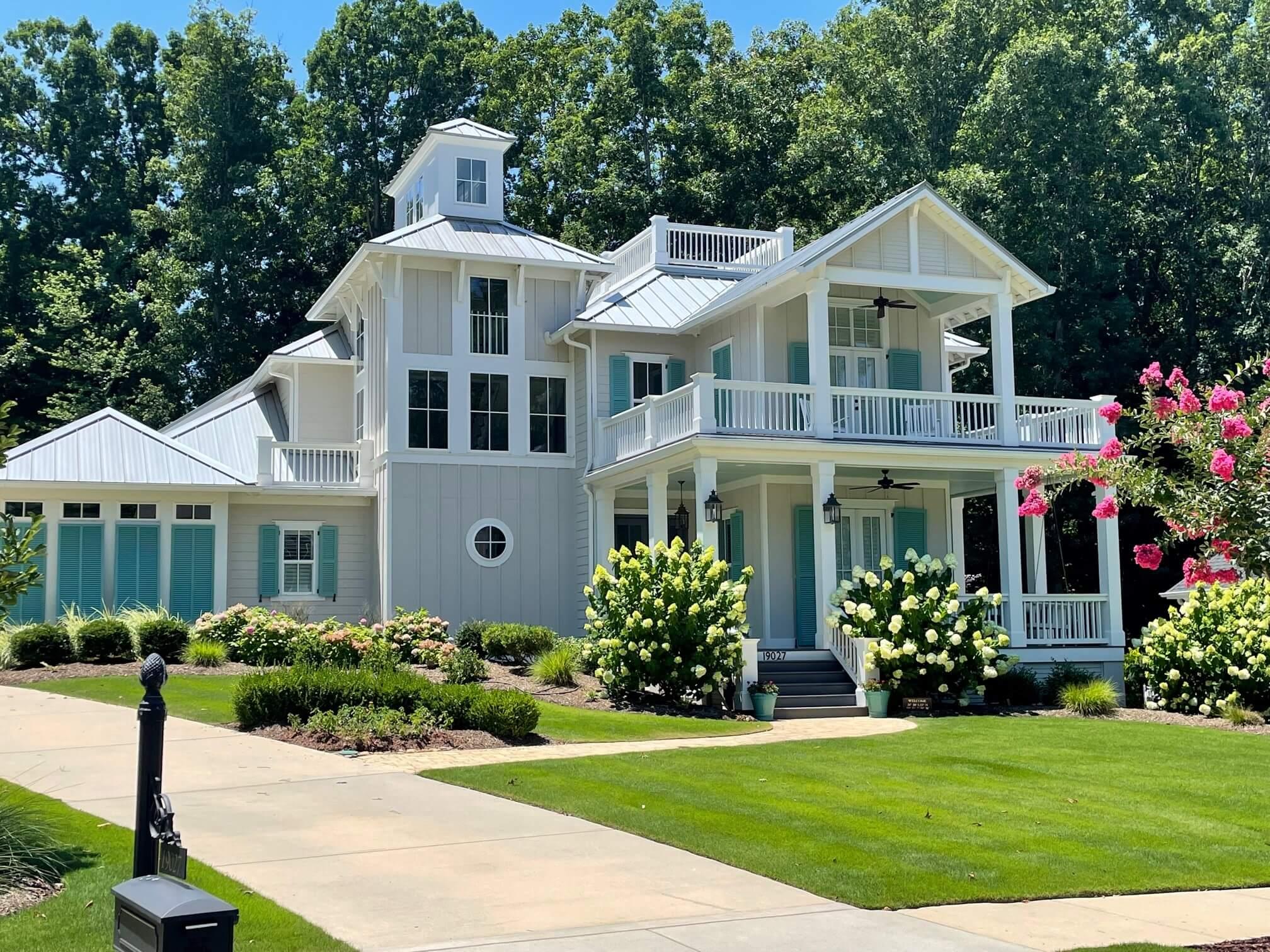 House plan exterior. Two-story with front porch, multiple balconies, and a cupola. Features include gabled rooflines and blue shutters.