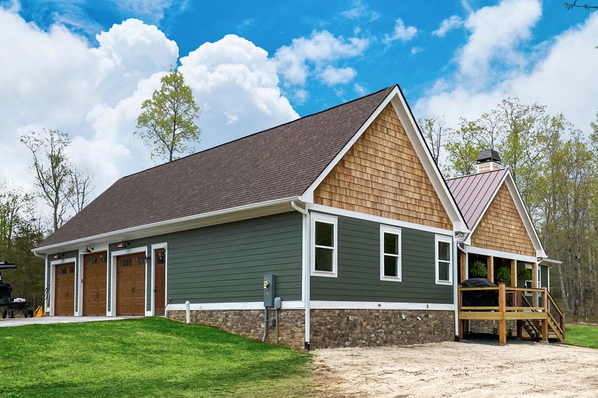A two-part building with a green exterior, brown shingle siding, and a brown roof. A lawn and a blue sky with fluffy clouds surround it.
