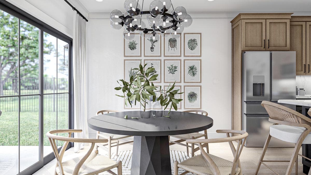 Dining area with round table, wishbone chairs, and gallery wall of botanical prints, adjacent to kitchen with island and stainless steel refrigerator.