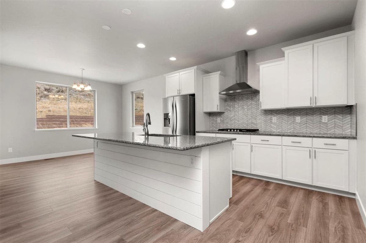 Modern kitchen with white shaker cabinets, granite island with sink, stainless steel appliances, and chevron tile backsplash.
