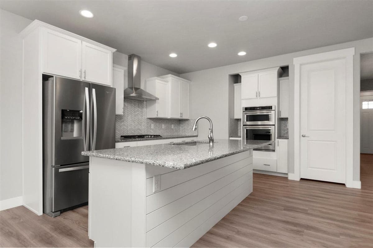 Kitchen with stainless steel refrigerator, granite island, and double ovens.