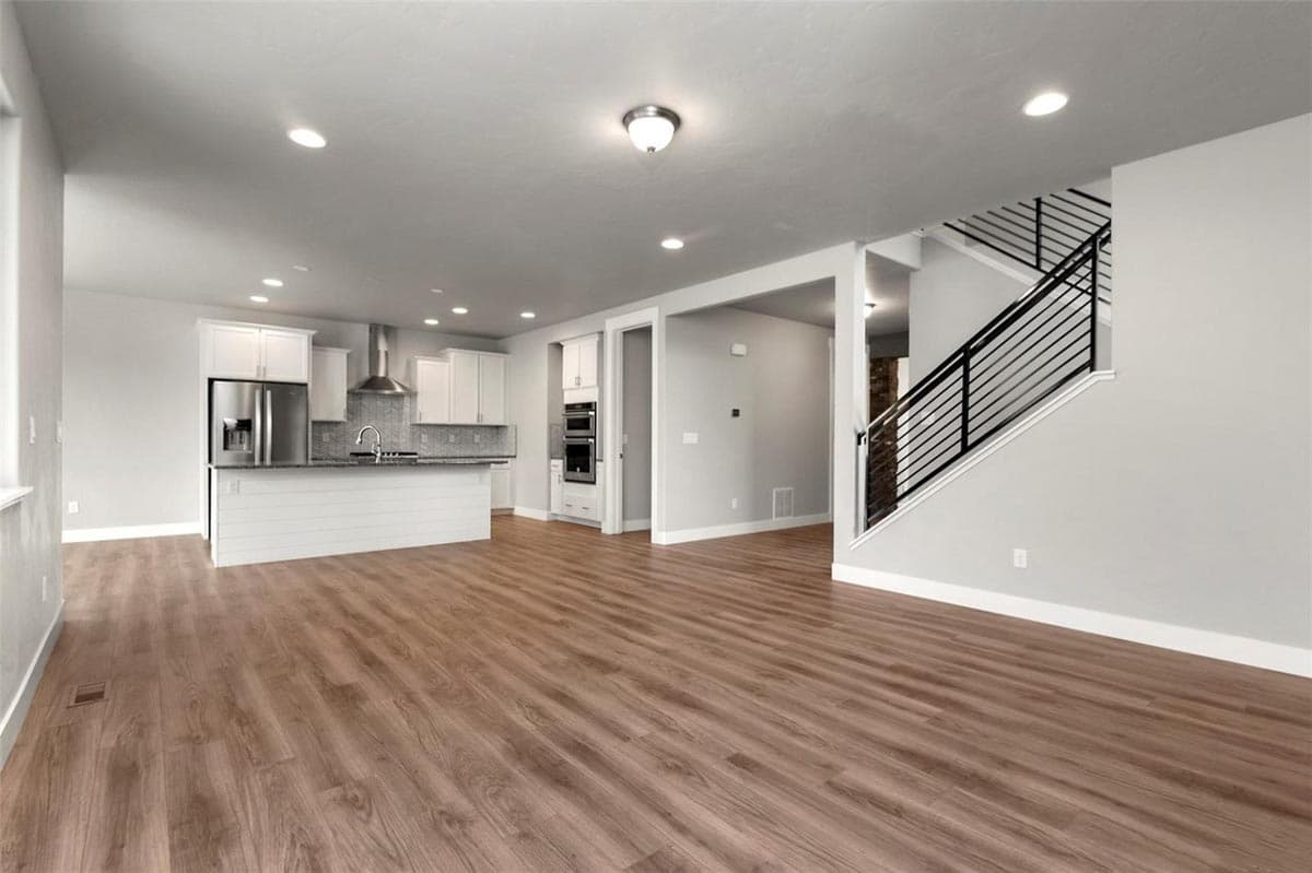 Open concept interior view shows kitchen with island and stairs with modern black railings leading to second floor.