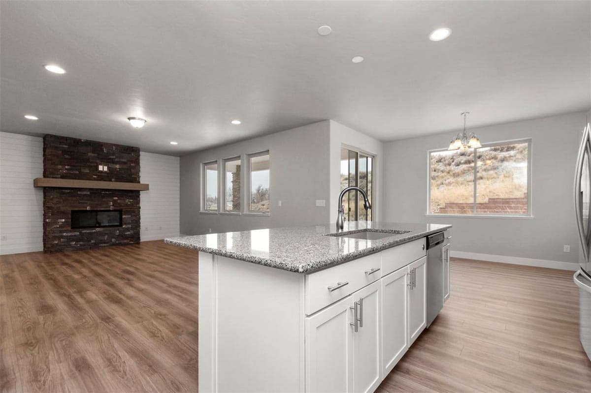 Open-concept living area featuring a stone fireplace and a kitchen island with granite countertops and a sink.