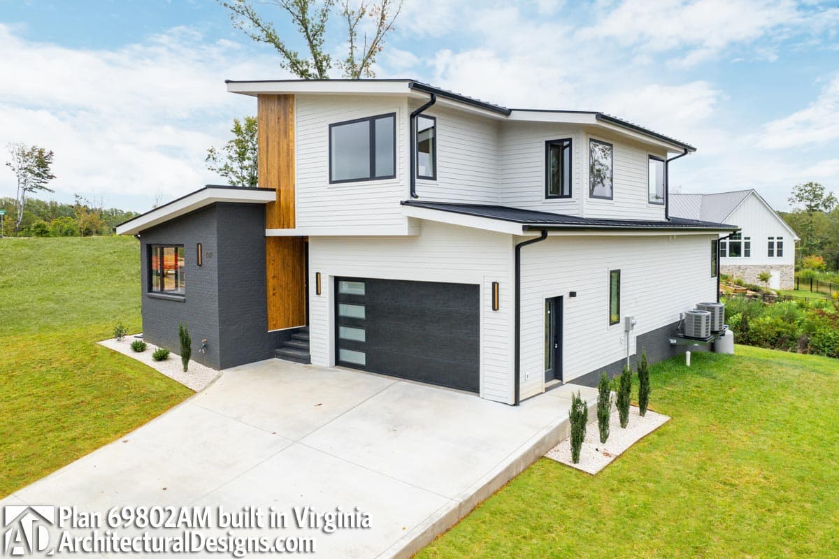 Modern two-story house plan exterior with asymmetrical gables, wood accents, dark brick base, and multi-pane garage door.