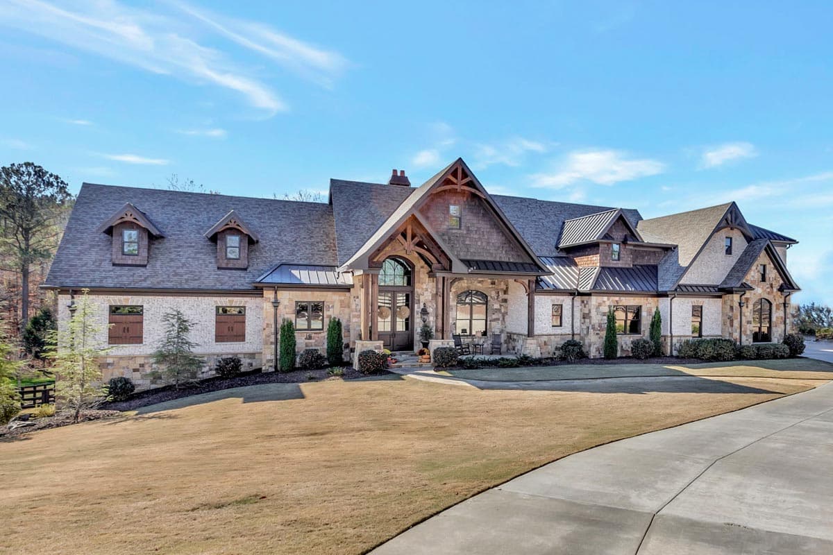 House plan exterior. Two-story, Craftsman-style home with multiple gable rooflines, dormers, and a covered porch. Stone and wood exterior.