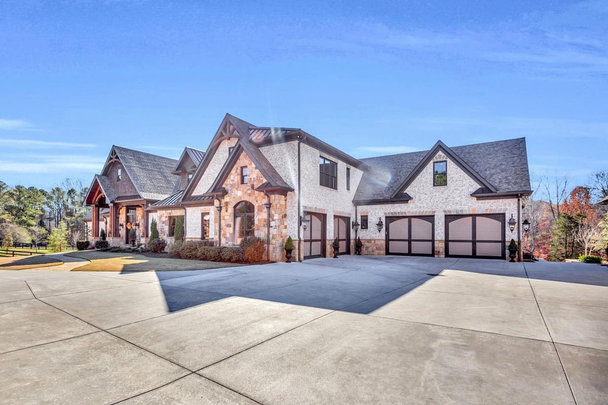 House plan exterior featuring a stone and brick facade, multiple gables, and a five-car garage with modern doors.