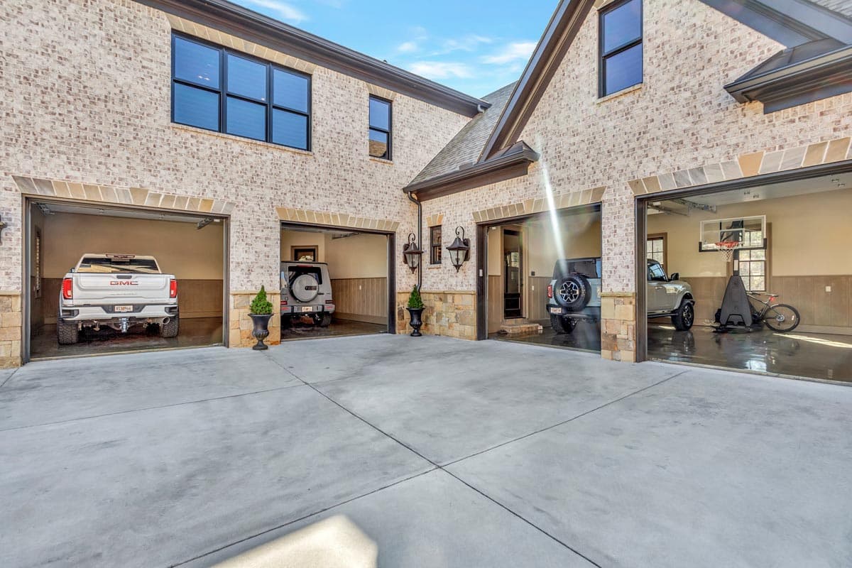 House exterior with light brick, stone accents, dark trim, and a four-car garage with glass doors.