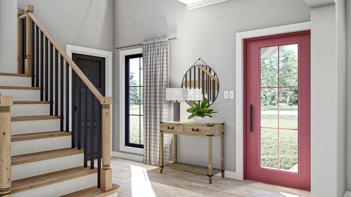 Interior view of a house entryway with a staircase, a red paneled door, and a console table.