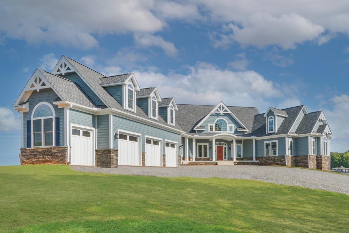 House plan exterior. Two-story home with a gabled roof, dormers, and a three-car garage. Features stone accents and arched windows.