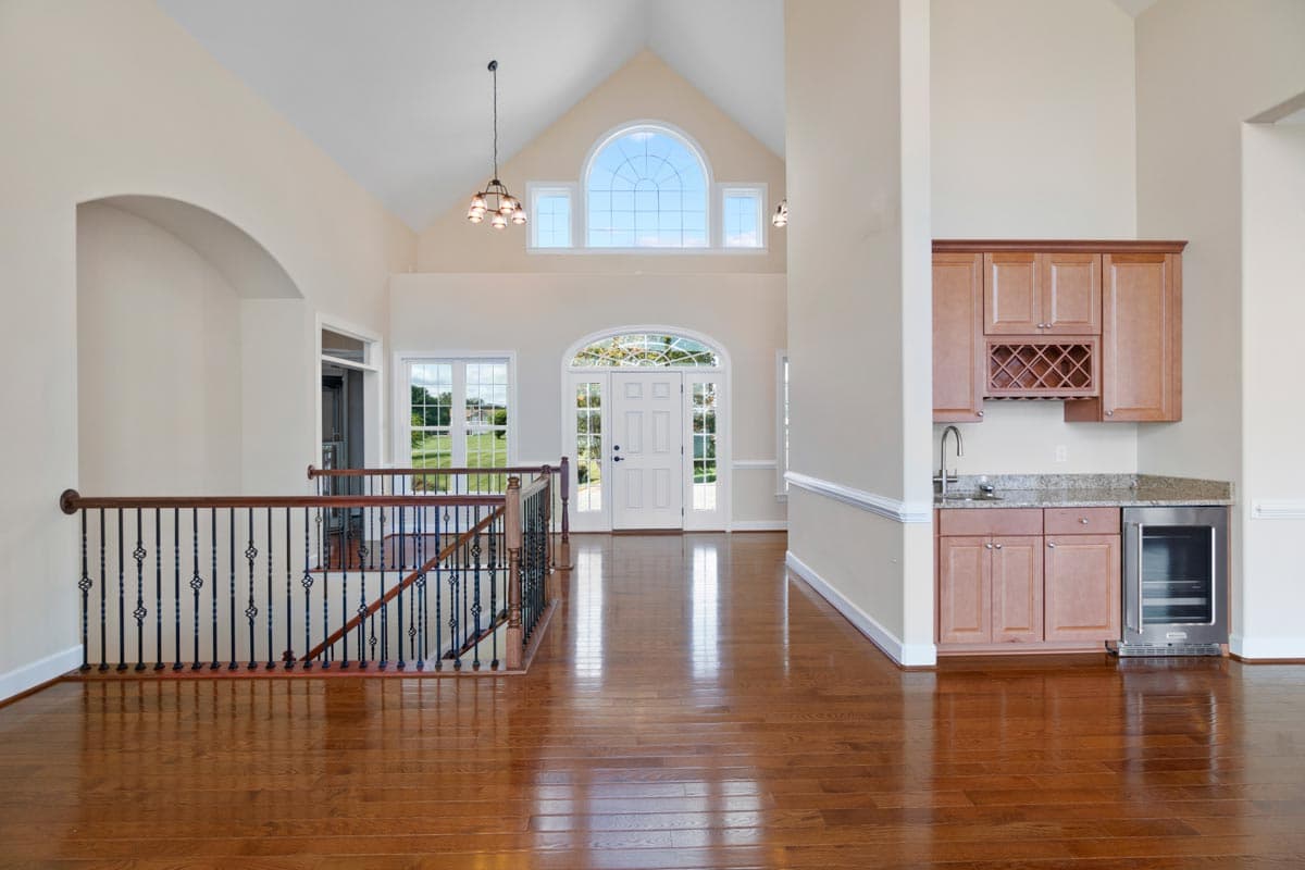 Interior view of a foyer with a vaulted ceiling, arched entryway, ornate banister, and wet bar.