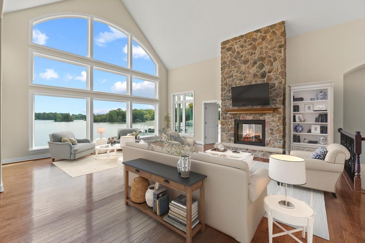 Great room with vaulted ceiling, floor-to-ceiling stone fireplace, and a wall of arched windows overlooking a lake.