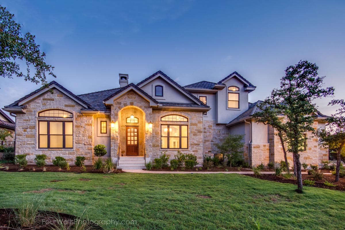 House plan exterior with stone facade, arched entry, multiple gables, and dormers. Two-story house with a dark roof and manicured lawn.