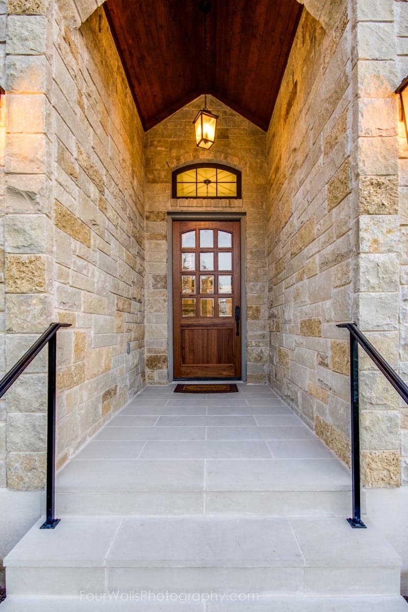 House plan exterior featuring a stone facade, arched entryway, wood door with glass panes, and a pendant light.