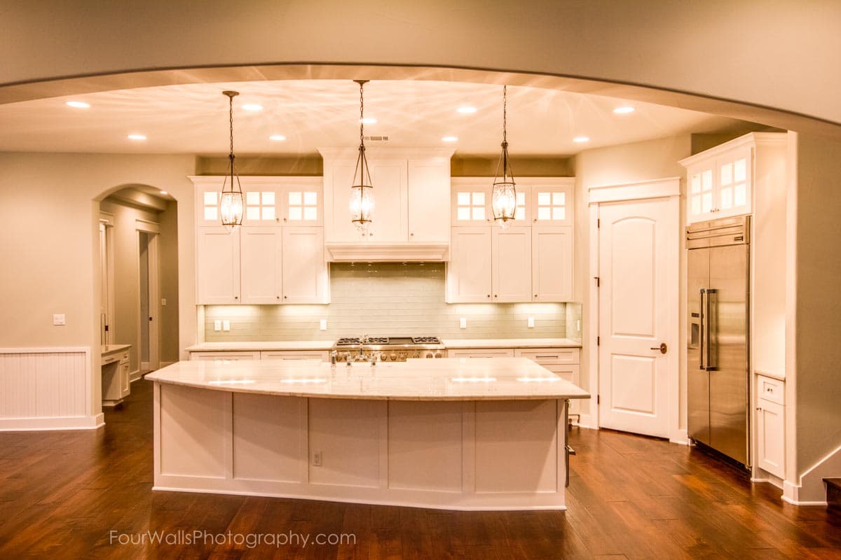 Kitchen with large island, white cabinets, stainless steel appliances, tile backsplash, and pendant lighting.