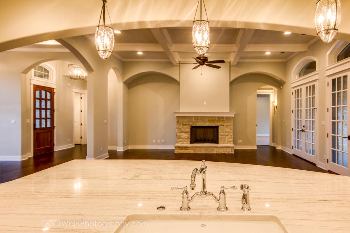 Interior rendering of a great room with a stone fireplace, coffered ceiling, arched doorways, and French doors.
