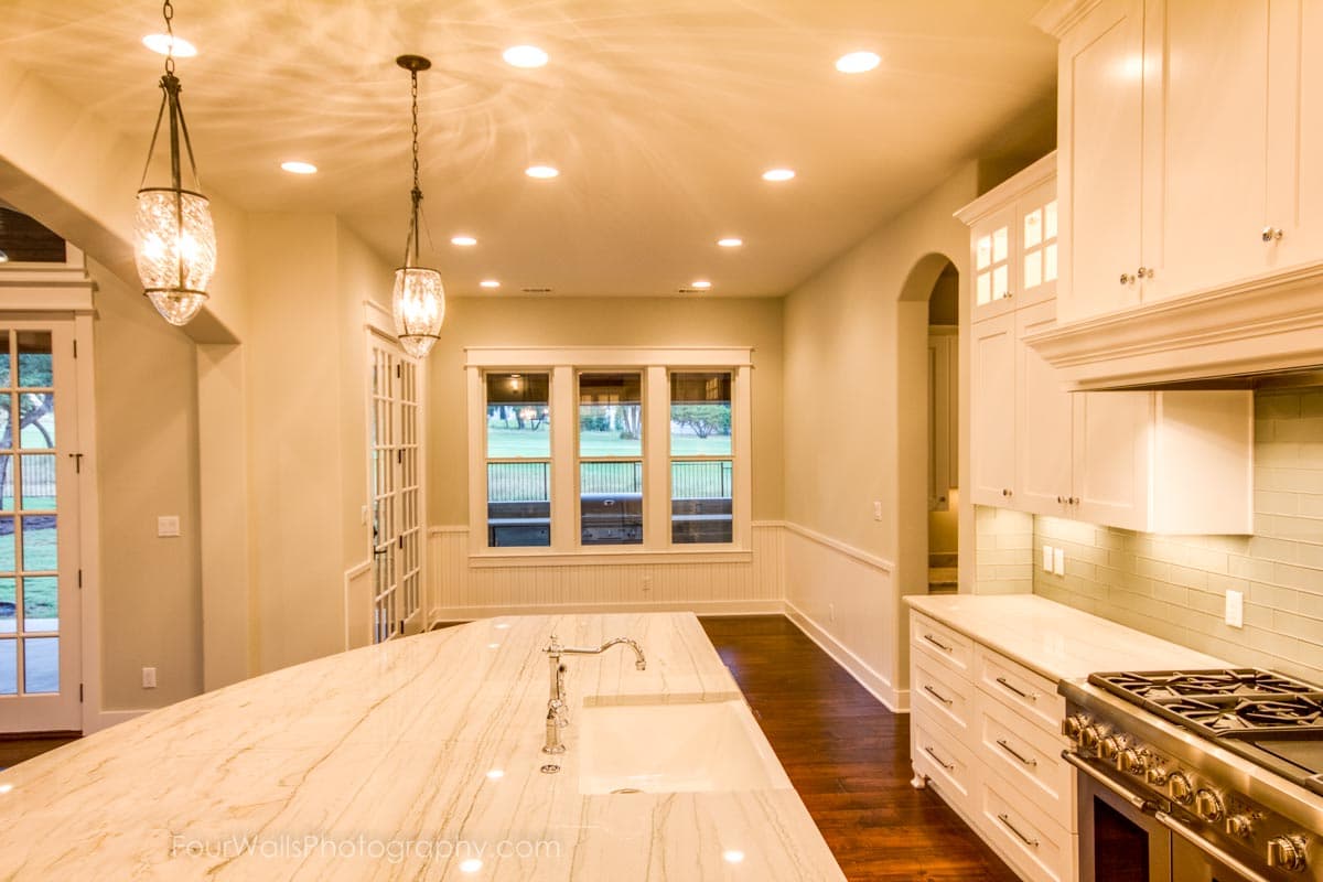 Kitchen with large marble island, white cabinetry, gas range, and subway tile backsplash.