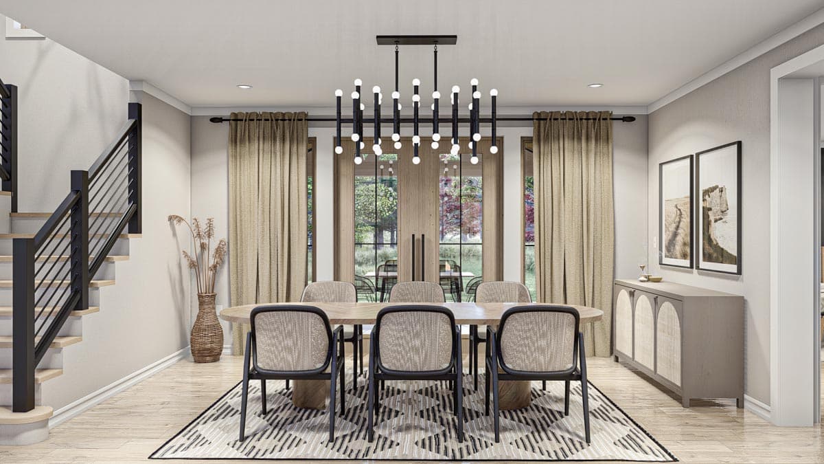 Dining room with oval table, cane-backed chairs, modern chandelier, and open staircase.