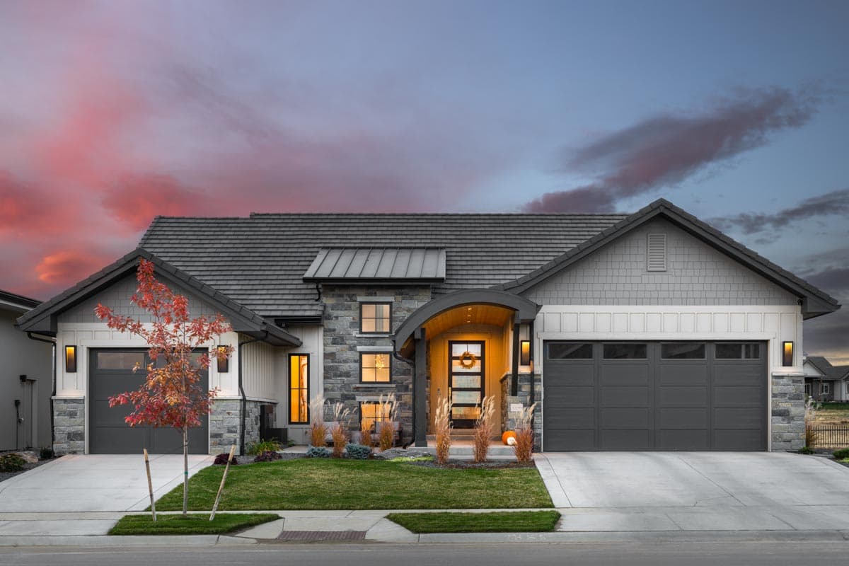House plan exterior. Modern farmhouse style with a single story, a curved portico, stone accents, and multiple gables. Features two attached garages.