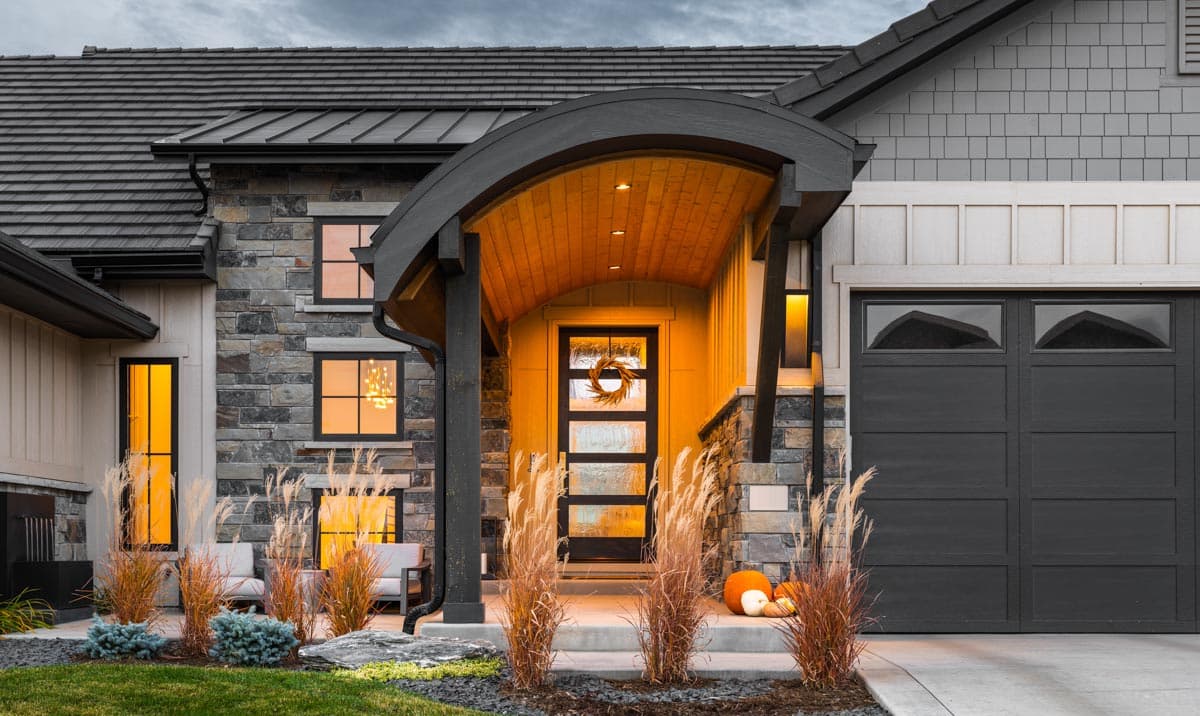 Modern house exterior with stone facade, arched covered entry, and dark garage door.