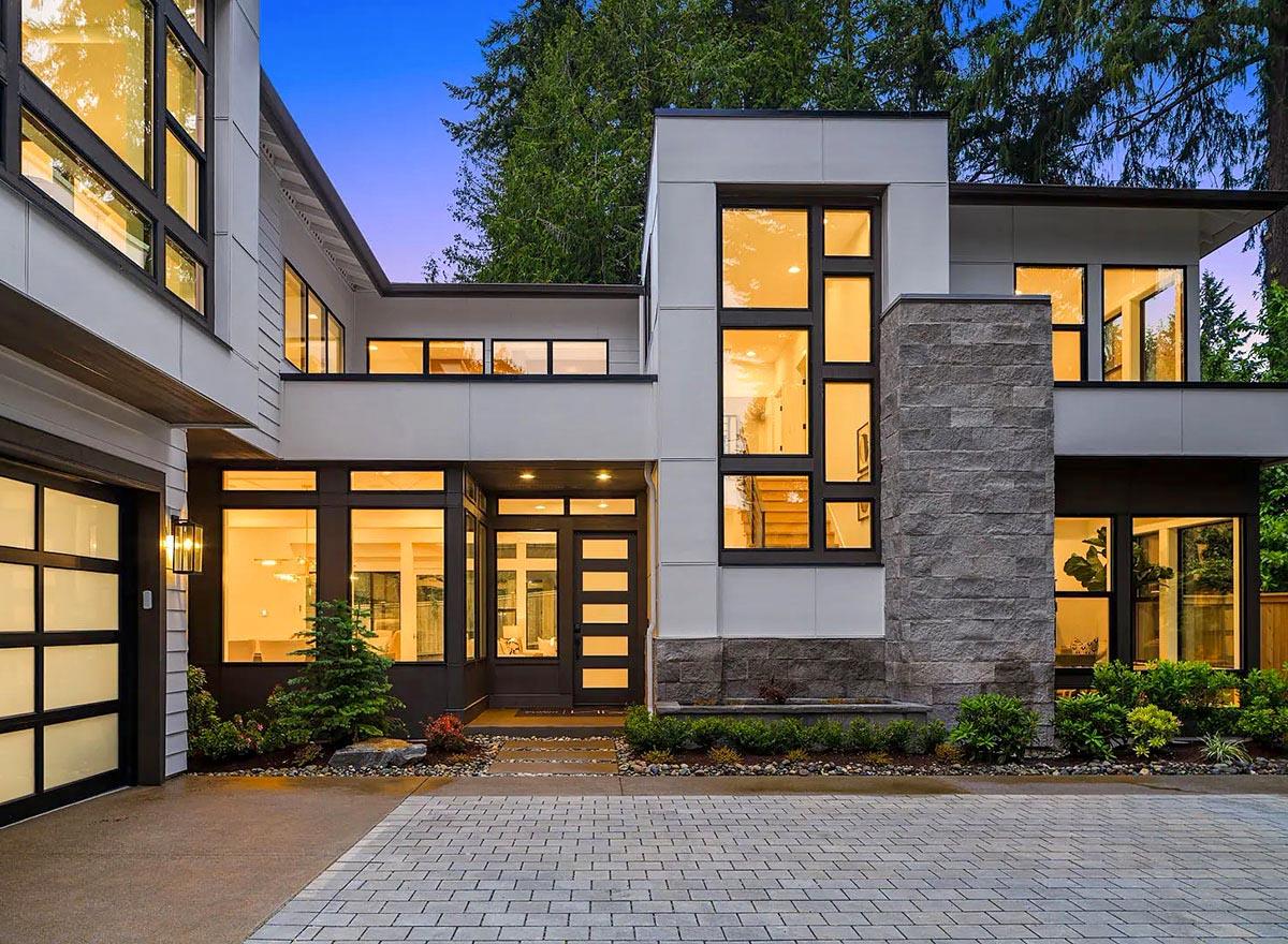 Modern house exterior with stacked stone chimney, multi-story windows, and attached garage.
