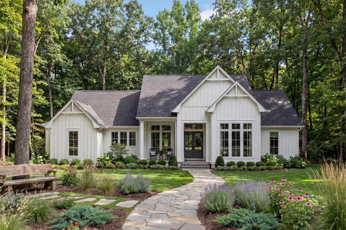 A white farmhouse with black trim is surrounded by a lush green lawn, trees, and a stone pathway leading to the front door.