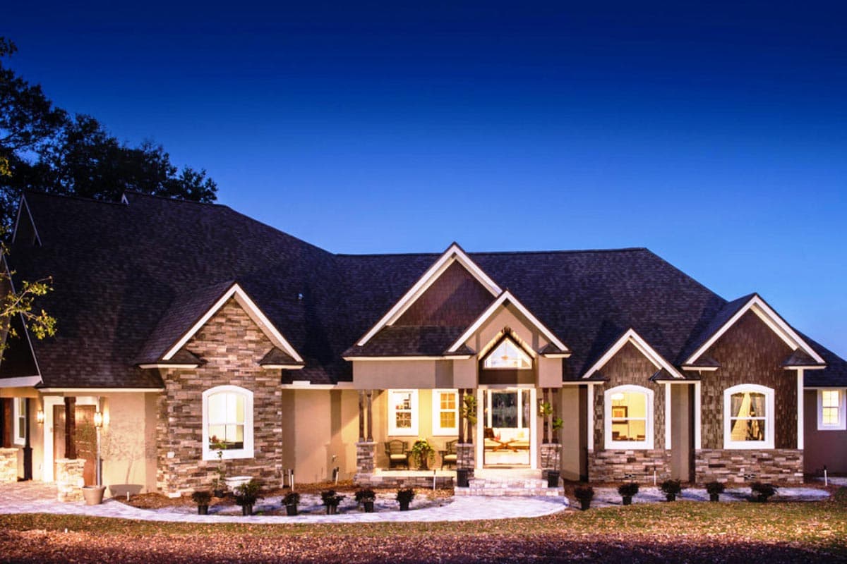 House plan exterior with stone veneer, multiple gables, and a covered porch. Features include a dark shingle roof and multiple dormers.
