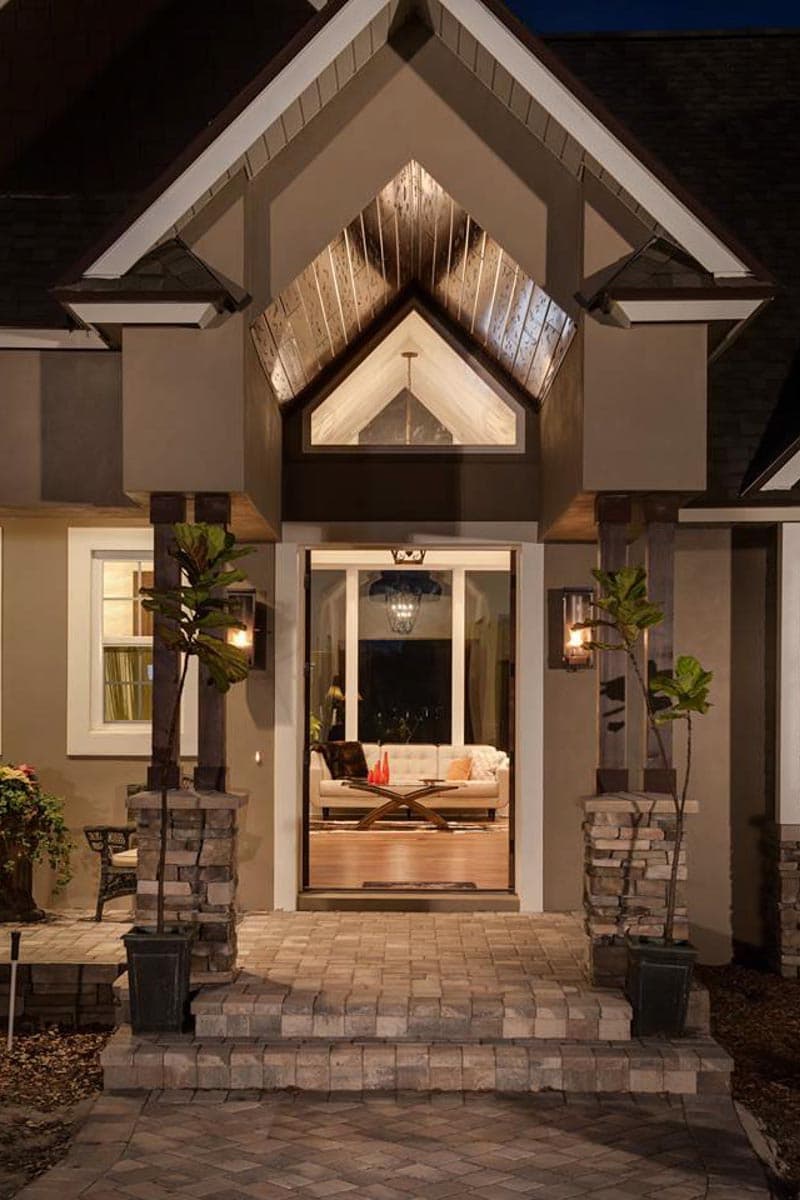 House plan exterior with a covered entry, stone column accents, pitched rooflines, and an upper gable window.