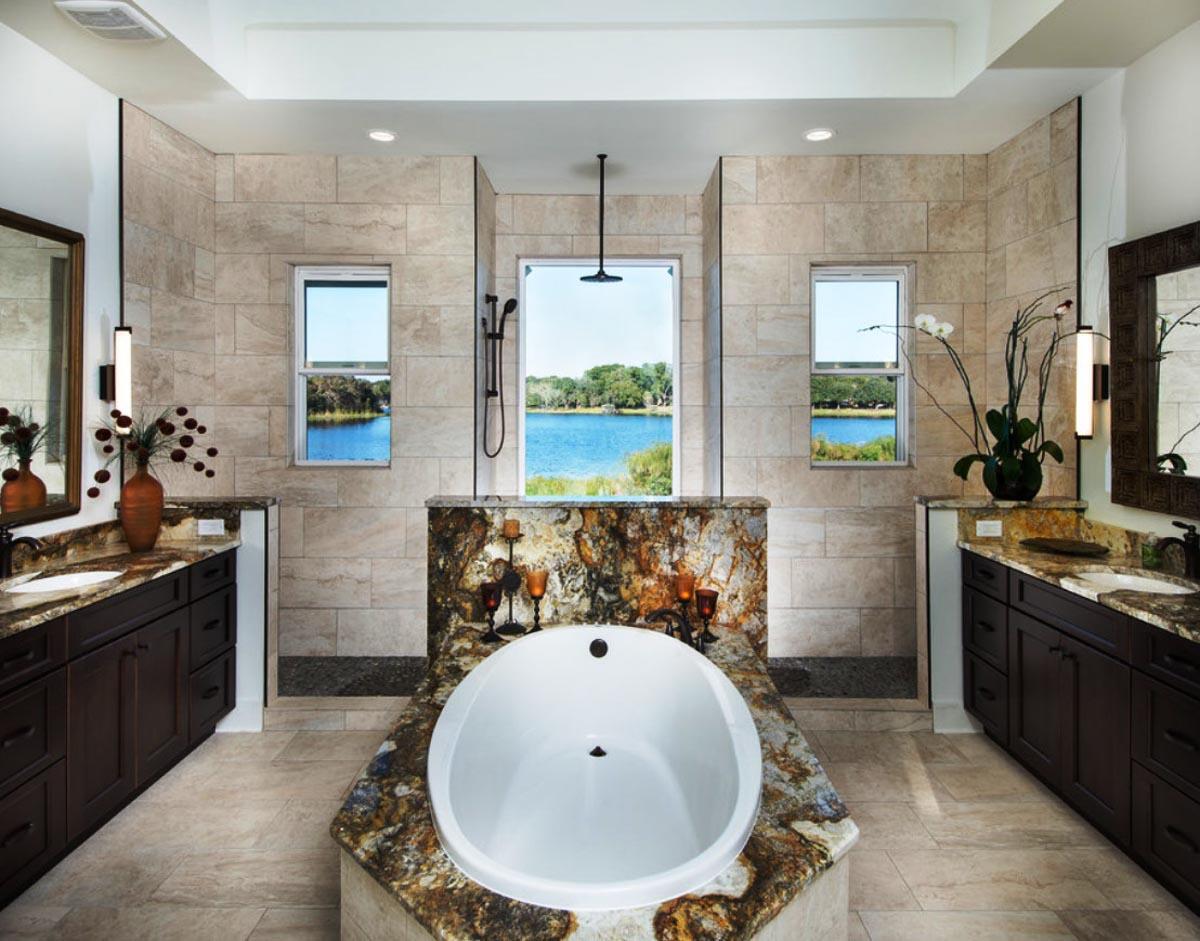 Bathroom with oval tub, dual vanities, tile shower, and windows overlooking water and trees.