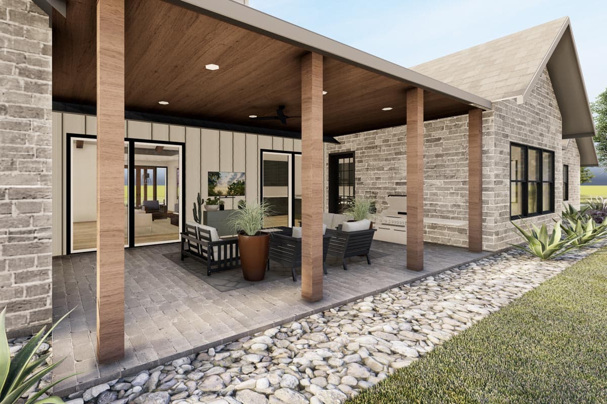 House plan exterior rendering showing covered patio with outdoor kitchen and seating area, brick exterior, and large windows.