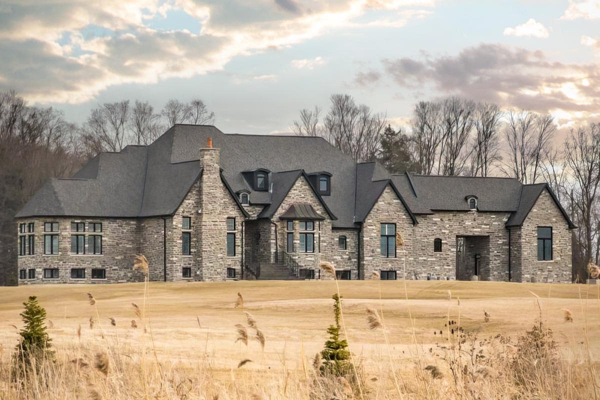 House plan exterior featuring a multi-gabled roof, stone facade, and dormers. The house has multiple stories with a large chimney.
