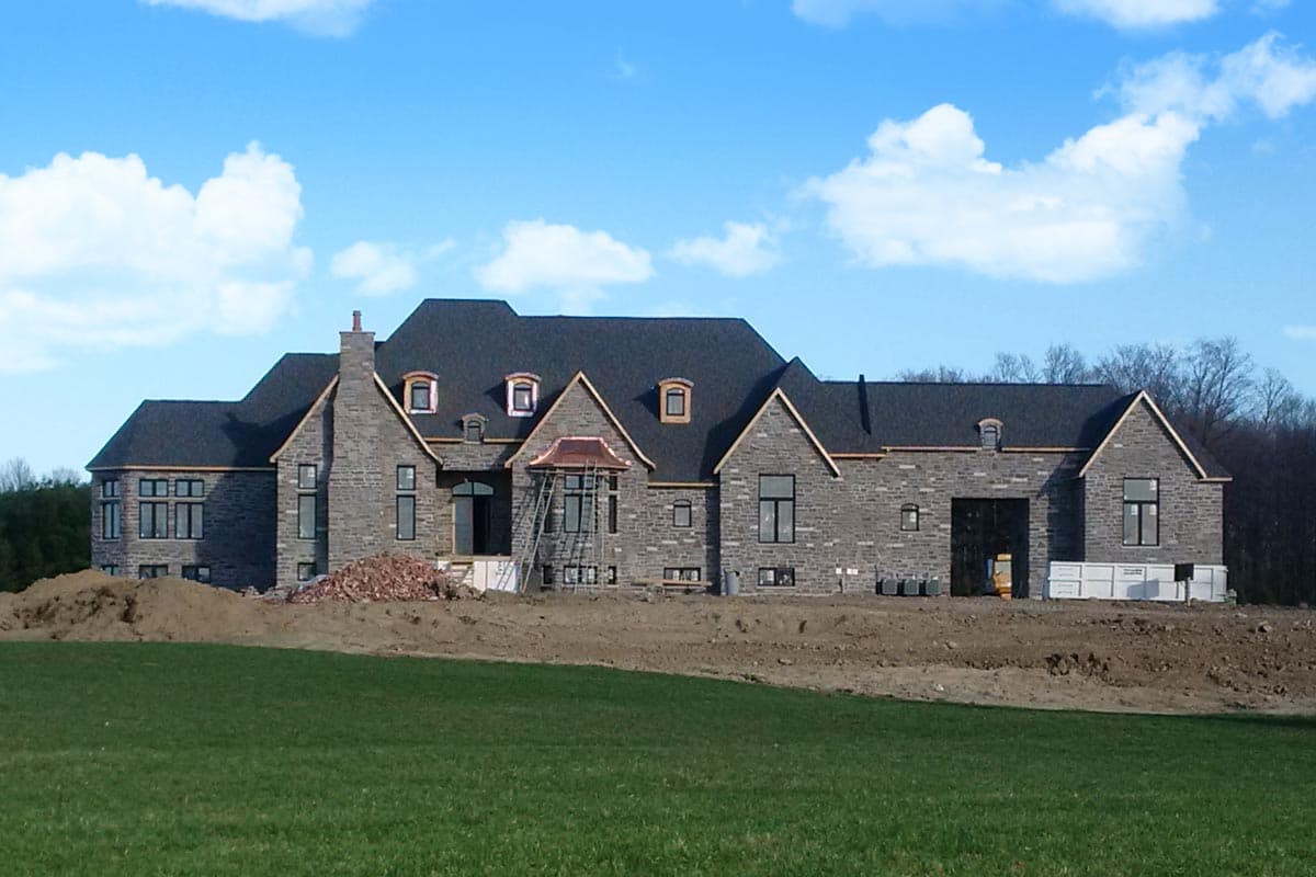House plan exterior featuring stone facade, multiple gables, dormers, and a complex roofline under construction.