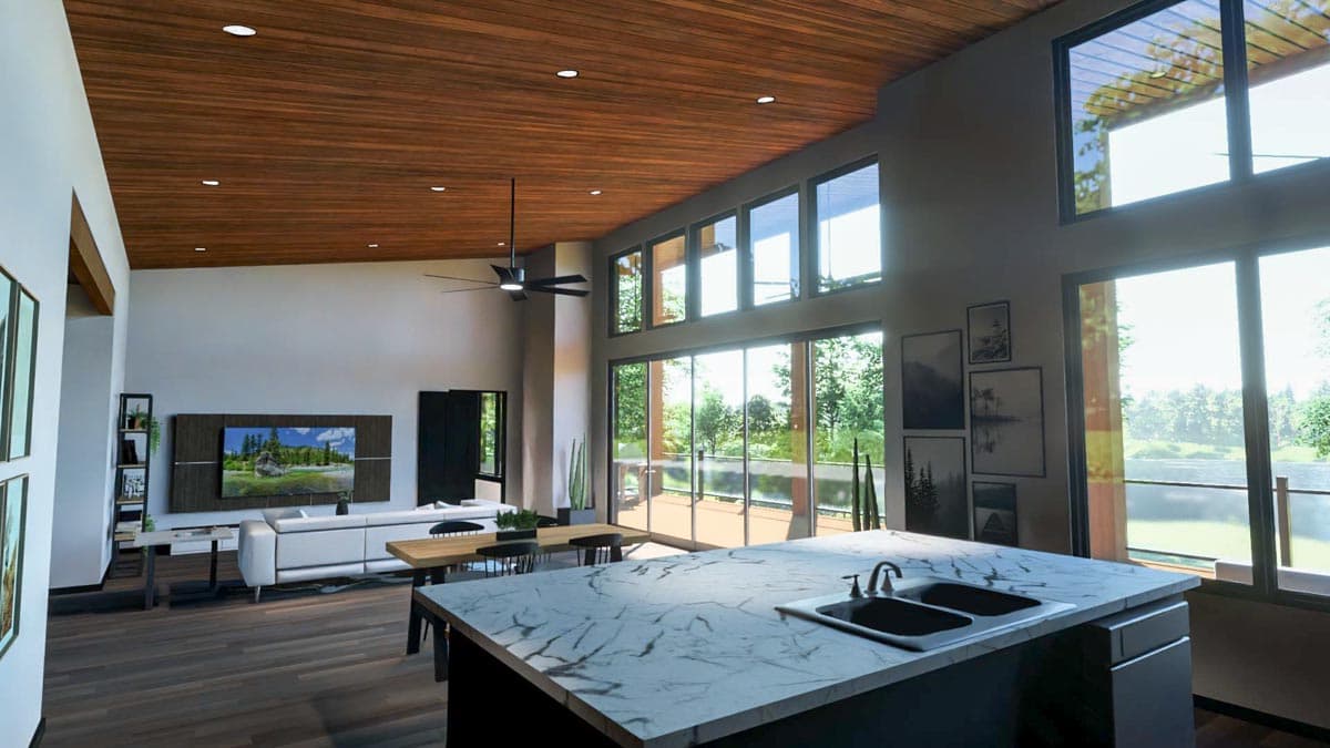 Modern open-plan living space with a kitchen island, large windows overlooking a deck, and wood ceiling details. A sofa faces a large-screen TV.