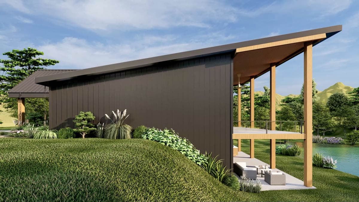 Modern house with a dark facade, wooden pillars supporting a porch overlooking a lake and forested area, lush landscaping in front.