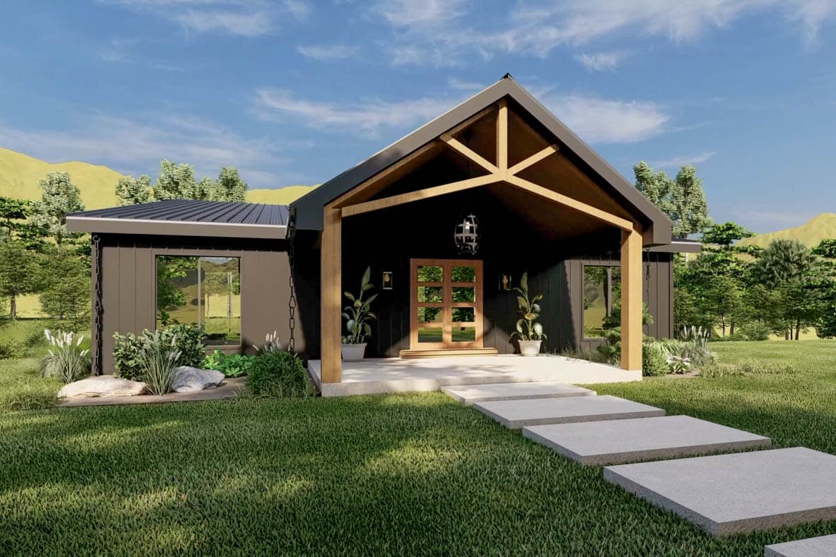 A modern, dark-sided house with a wooden porch and entrance, stone pathway through the front lawn, and surrounding trees with a mountain background.