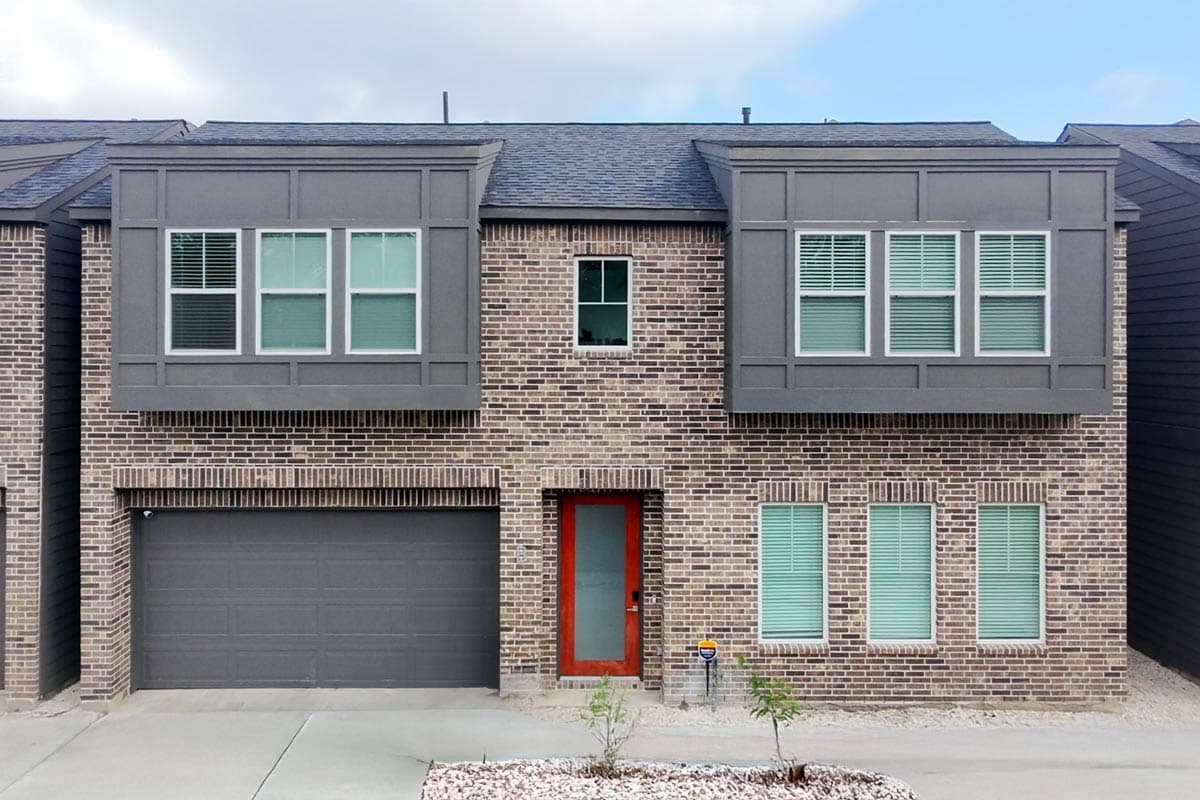 House plan exterior: two-story modern design with brick facade, prominent gray box elements, garage, and orange-framed front door.