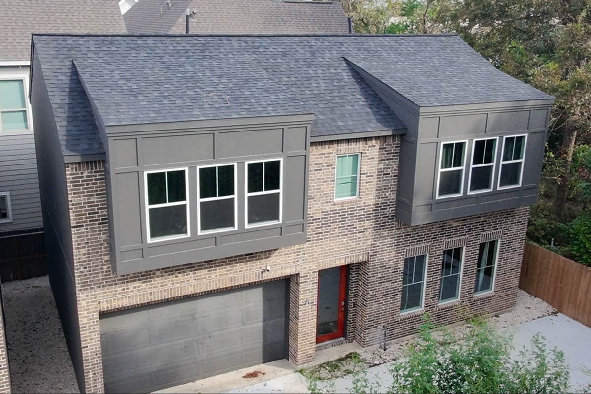Two-story house plan exterior with brick facade, dark pitched roof, inset bay windows on second story, and attached garage.