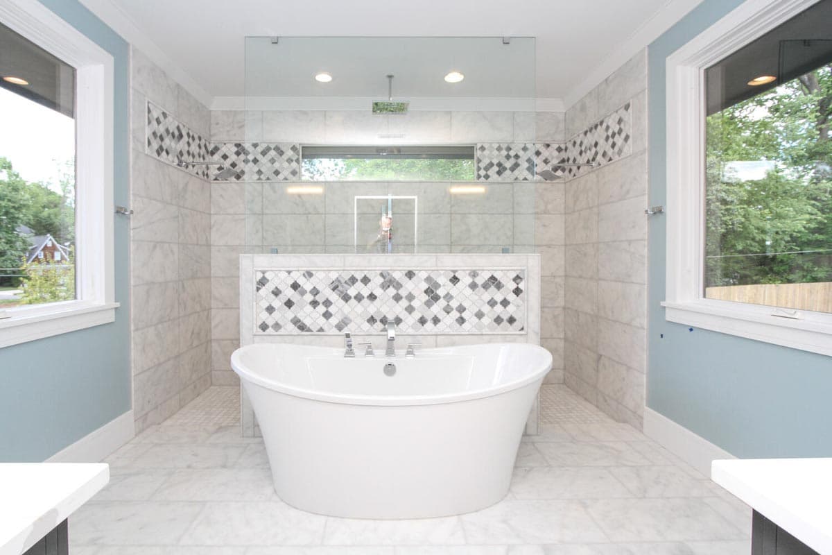 Bathroom with freestanding tub, marble tile walls and floors, and glass-enclosed shower with rainfall showerhead.